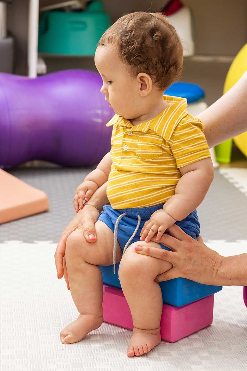 Ein Kleinkind macht sitzend Gleichgewichtsübungen auf einem Gymnastikball